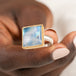 Gold and silver ring with a moonstone held in hand against a white background