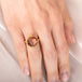 Gold ring with a face design carved into sunstone on a person's finger