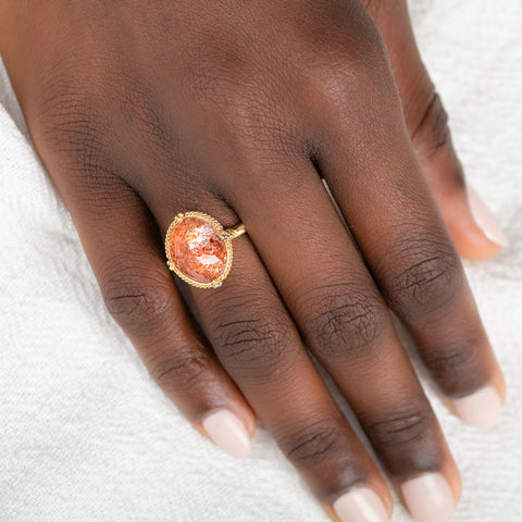 Gold ring with a sunstone stone on a person's finger against a neutral background