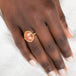 Gold ring with a sunstone stone on a person's finger against a neutral background