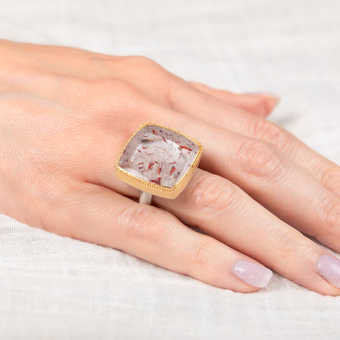 Hand wearing a gold and silver ring with a super 7 stone on a light background