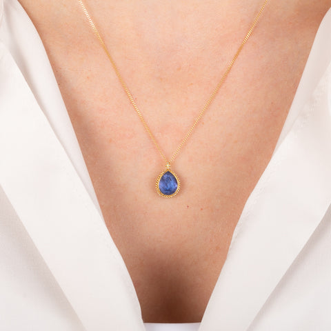 Gold necklace with a blue teardrop tanzanite on a person
