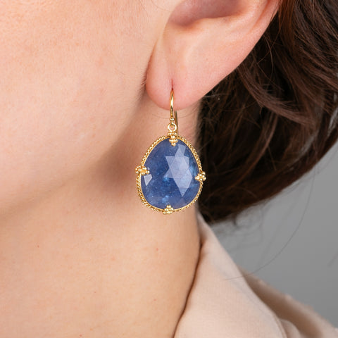 Gold earrings with blue tanzanite gemstones worn by a person