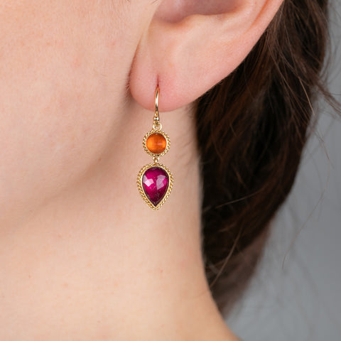 Gold earrings with tourmaline and fire opal gemstones worn on a person