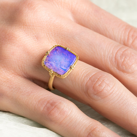 Gold ring with a purple boulder opal stone on a hand