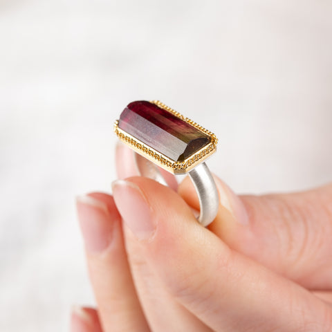 Close up of hand holding a watermelon tourmaline ring with gold bezel and silver band
