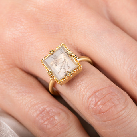 Gold ring with a dendritic quartz stone featuring natural inclusions on a hand