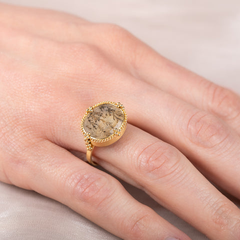 Gold ring with a dendritic quartz stone and intricate design on a hand