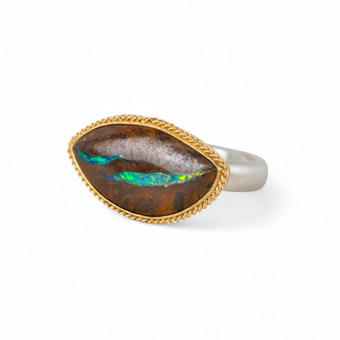 Ring with an opalized wood stone, gold setting and silver band on a white background