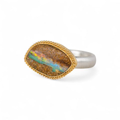 Ring with an opal stone, gold setting and silver band on a white background