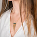 A person wears a handcrafted fine jewelry necklace featuring a black opal gemstone and 18k gold tassel adornment