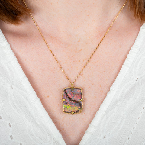 A model wears an 18k yellow gold and boulder opal gemstone necklace.