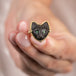 Close up of a model holding an 18k yellow gold and onyx cat ring.