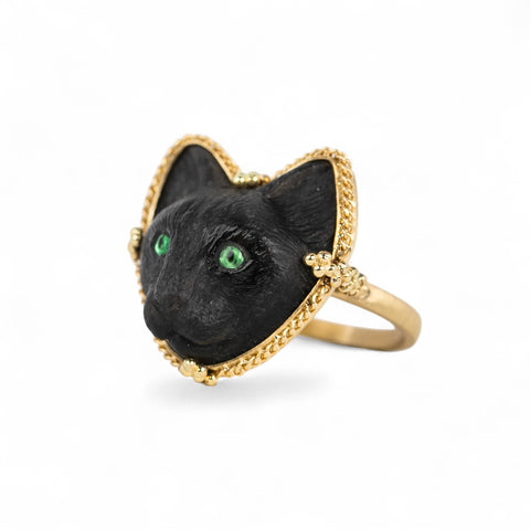 Side view of an 18k yellow gold ring featuring a black cat face carved from onyx with green eyes.