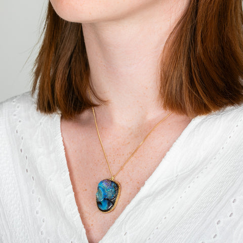 A model wears a carved boulder opal gemstone and 18k yellow gold necklace.