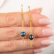 A pair of gold dangle earrings with round iridescent blue and green boulder opal stones, shown hanging from a person's fingers against a clean white background.