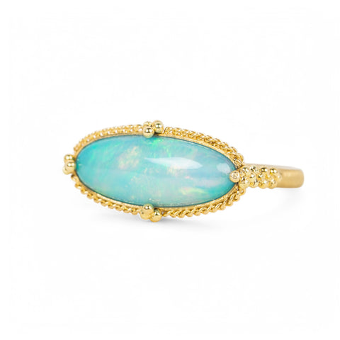 A handmade ring featuring an oval ethiopian opal gemstone in an 18k gold setting on a white background.