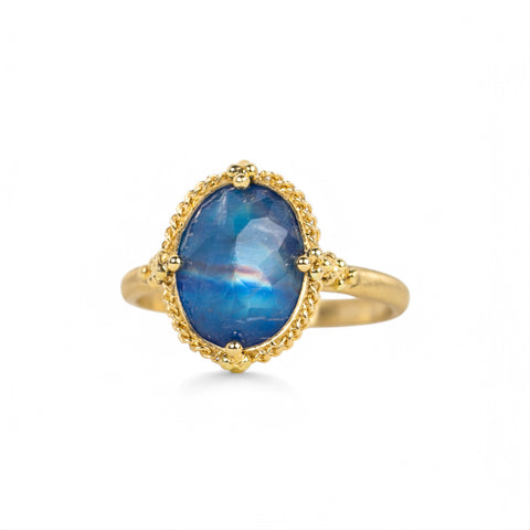 An oval-shaped blue Moonstone gemstone ring with a faceted surface, set in a handcrafted 18k yellow gold bezel.