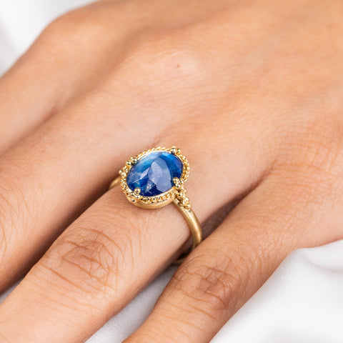 A model wears an oval-shaped blue Moonstone gemstone ring with a faceted surface, set in a handcrafted 18k yellow gold bezel.