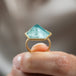 A model holds an 18k yellow gold and aquamarine ring from a side angle showing its three dimensional nature.