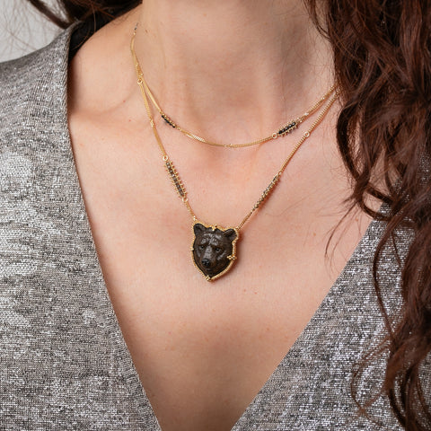 A model wearing a handcrafted grizzly bear necklace featuring a carved jasper gemstone, 18k yellow gold and grey diamond embellishments.