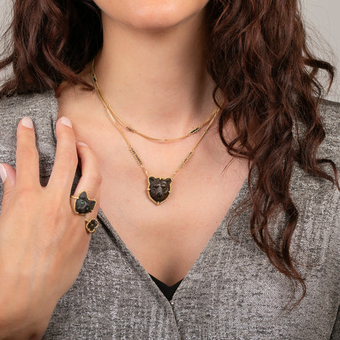 A model wearing a carved grizzly bear gemstone and 18k gold necklace with another 18k gold chain necklace embellished with black diamonds.