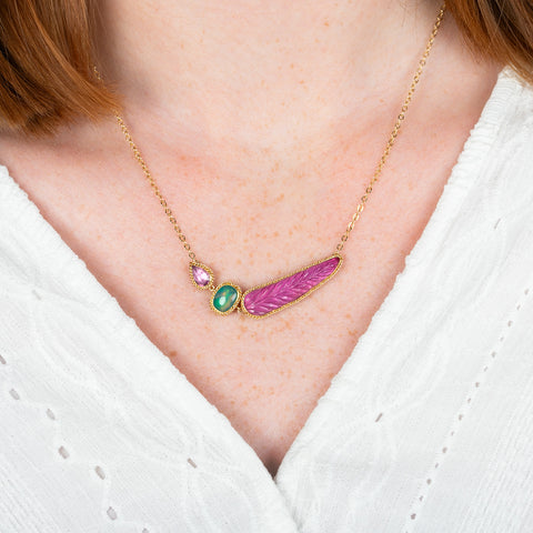 A model wears an 18k yellow gold necklace featuring a ruby, ethiopian opal, and carved feather tourmaline gemstone.