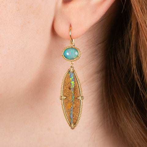 A model wears a long drop earring featuring opalized wood and opal set in handmade 18k yellow gold bezels.