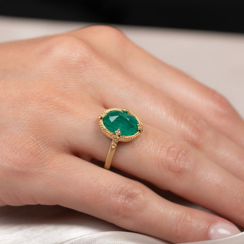 A model wears an 18k yellow gold and emerald ring featuring gold prongs that hold the emerald in place.