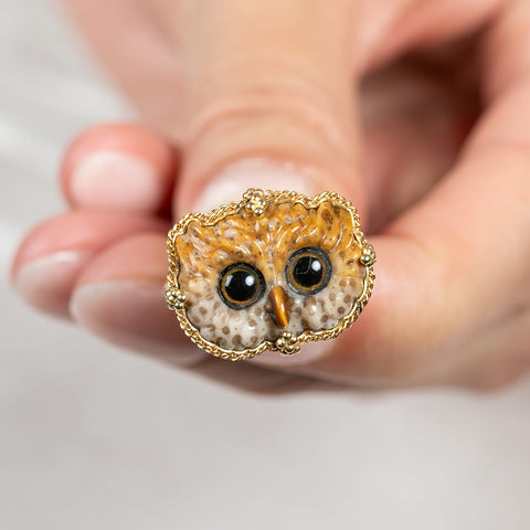 A close up of a model holding an owl ring made of 18k yellow gold and hand-carved leopard jasper.
