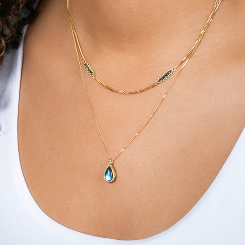 A model wears a teardrop-shaped moonstone pendant set in an 18k yellow gold bezel, suspended from a matching gold chain.