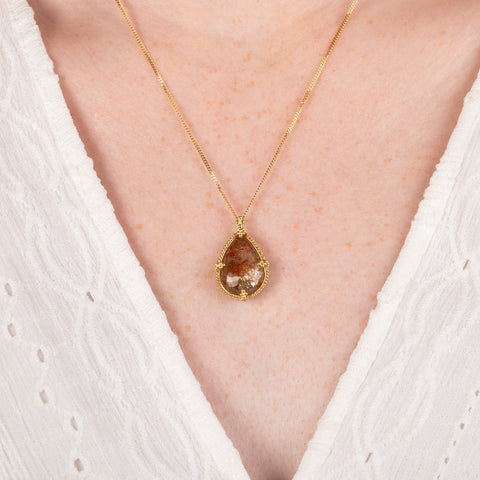 A close up of a model wearing a teardrop shaped Spessartite and 18k gold necklace.