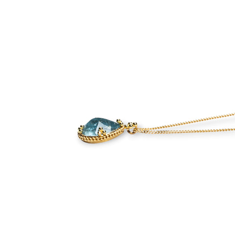 A side-view of a teardrop shaped aquamarine stone necklace set in 18k yellow gold.