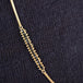 A close-up of a long 18k yellow gold necklace that features an off-center row of black diamond beads.