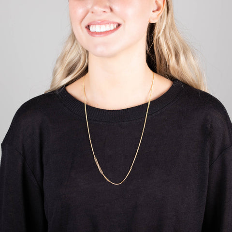 A model wears a long 18k yellow gold chain necklace that features an off-center row of woven champagne diamond beads.