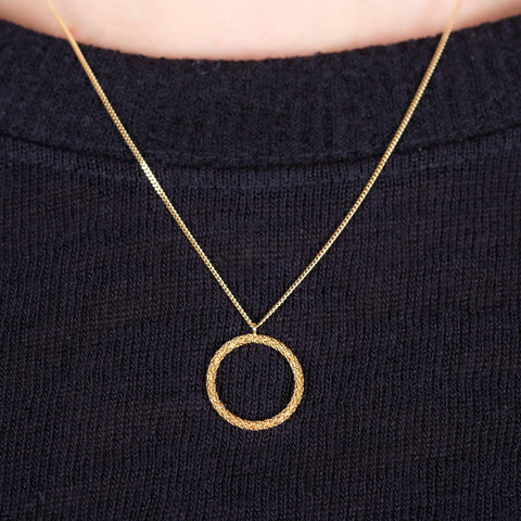 A close up of an 18k yellow gold  circular pendant crafted in chain to create a stardust-like effect