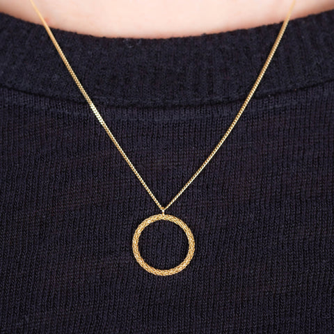 A close up of an 18k yellow gold circular pendant crafted in chain to create a stardust-like effect