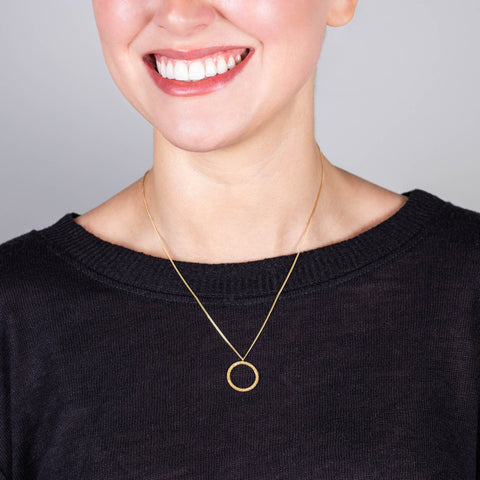 A model wears a delicate 18k yellow gold chain necklace with a small circle pendant crafted in chain to create a stardust-like effect
