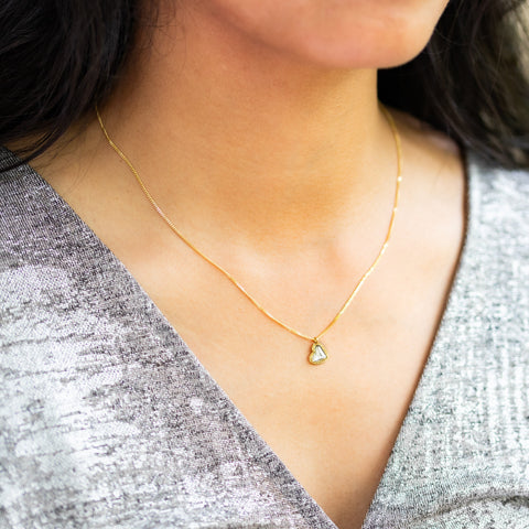 A close up of a heart-shaped Diamond pendant suspended from an 18K yellow gold chain. Handmade gold bezel with braided detail and granulation. Handmade in New York.
