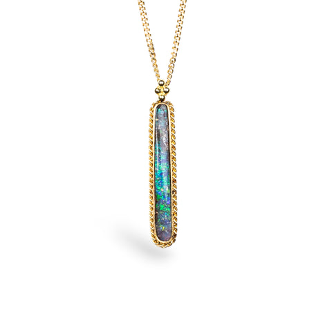 An Elongated Boulder Opal pendant is set in an 18k yellow gold bezel, and suspended from an 18K yellow gold chain. Opal displays enchanting blues, purples, and greens, set in a unique one-of-a-kind design with braided detail.