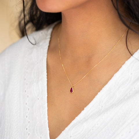 A model wears this geometric Ruby pendant on an 18K yellow gold chain. Handmade gold bezel features braided detail. Handmade in New York.