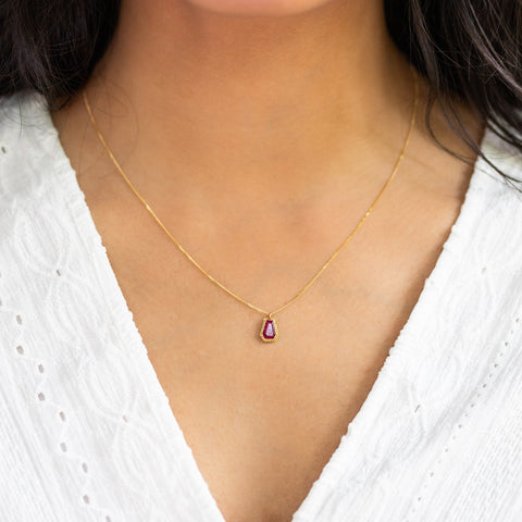 A model wears this geometric Ruby pendant on an 18K yellow gold chain. Handmade gold bezel features braided detail. Handmade in New York.