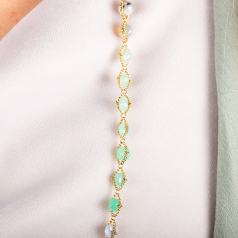 A close up of a mixed opal bead necklace featuring teal stones that are woven with 18k yellow gold chain.