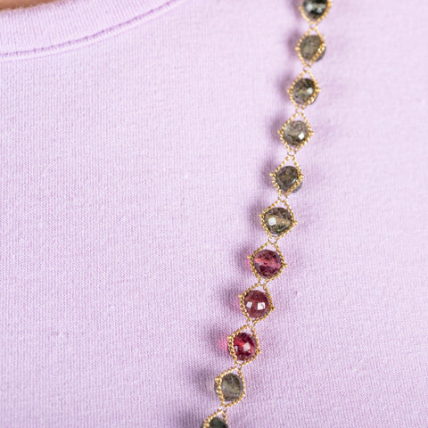 A close-up of a green and pink tourmaline bead necklace woven with 18k yellow gold chain