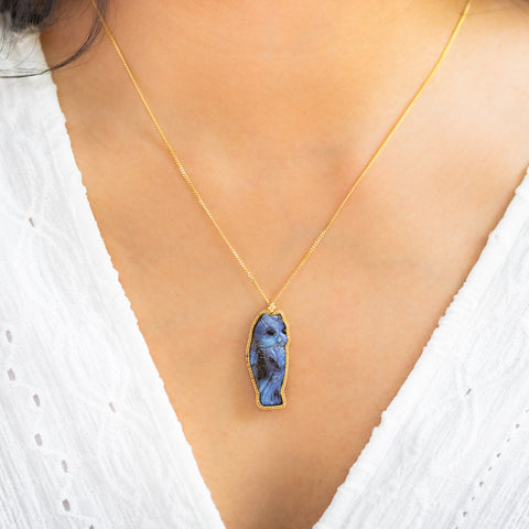 A model wears a Boulder Opal owl pendant in 18K yellow gold, meticulously carved with intricate details in feathers, eyes, and beak. Set in a handmade gold bezel with braided detail, suspended from an 18K yellow gold chain.