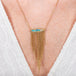 A person wears a handcrafted necklace made of opalized wood and 18k gold with a gold tassel adornment