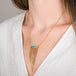 A person wears a handcrafted necklace made of opalized wood and 18k gold with a gold tassel adornment