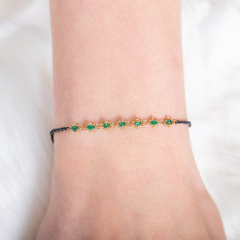 A model wears an oxidized sterling silver bracelet that features a row of green emeralds suspended in 18k yellow gold chain in the center.