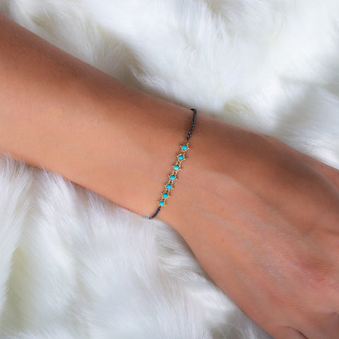 A model wears an oxidized sterling silver bracelet that features a row of turquoise beads suspended in 18k yellow gold chain in the center.