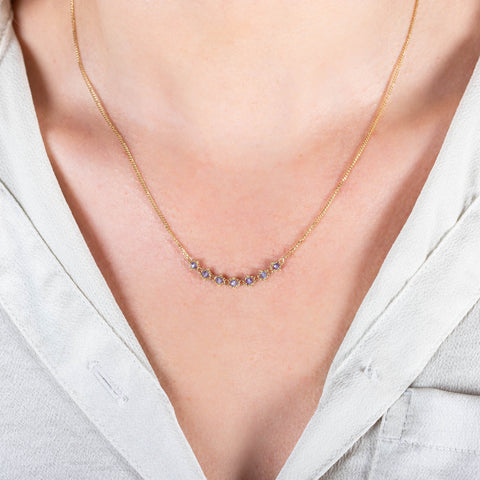 A model wears a delicate 18k yellow gold necklace with a row of woven tanzanite beads in the center.